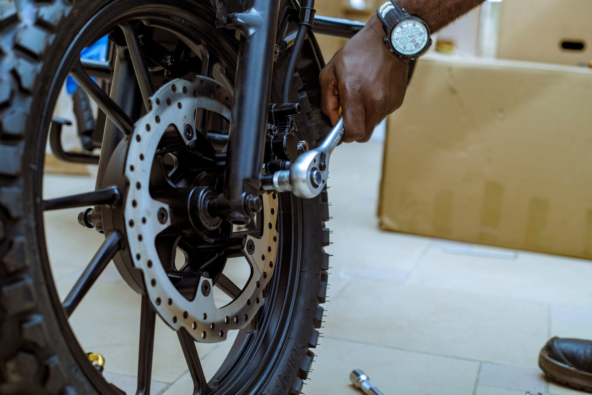 An Ehu technician tightens a motorcycle’s front brake caliper, ratchet wrench in hand.