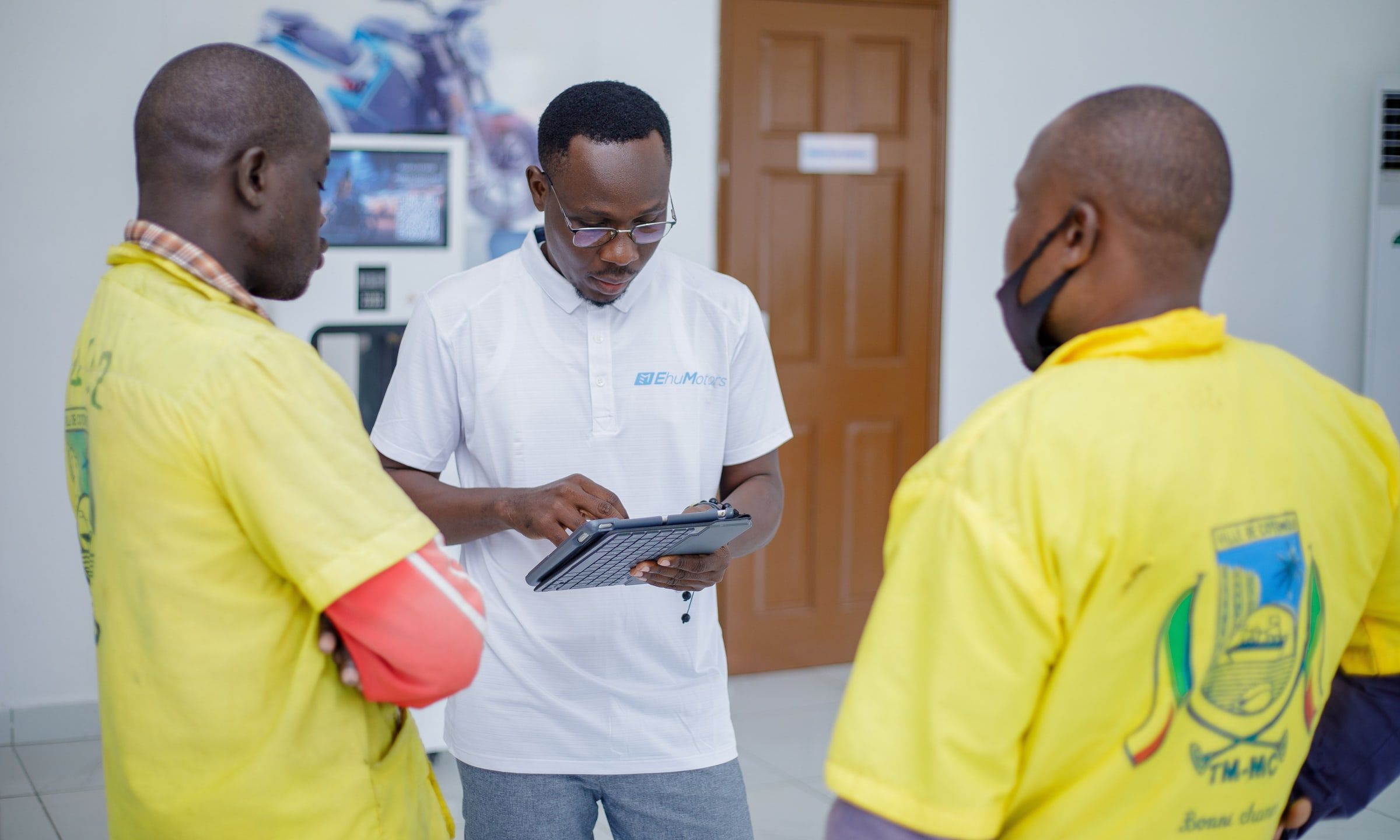 An Ehu advisor, tablet in hand, with two motorcycle-taxi drivers at the showroom.