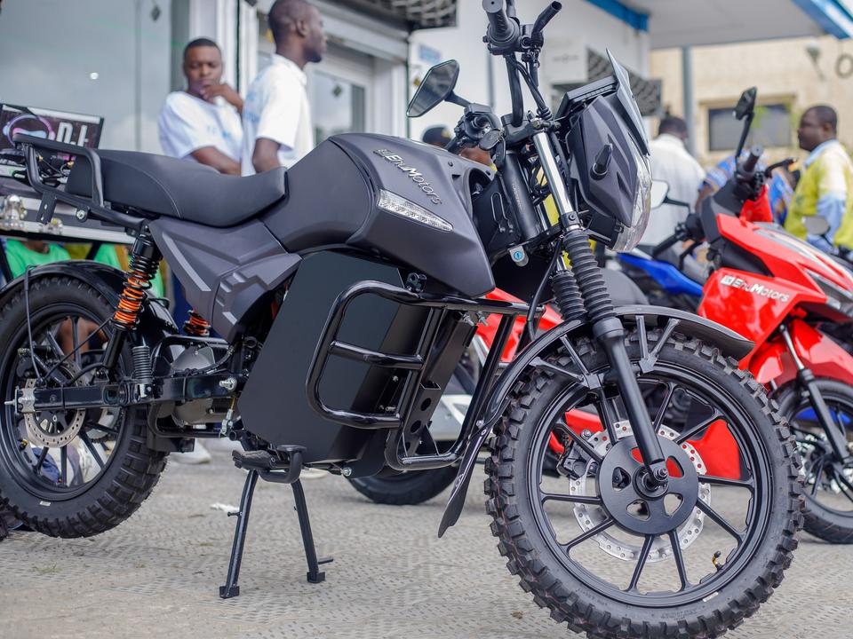 A Finesse, a black Ehu electric motorcycle, parked outside the Cotonou showroom, with riders in yellow vests behind it.